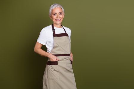 Photo of charming positive woman wear apron serving coffee smiling empty space isolated khaki color backgroundの写真素材