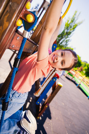 Vertical photo of adorable funny little girl have fun outside hang play playground activity enjoy summer weekend pastime fresh air outdoorの写真素材