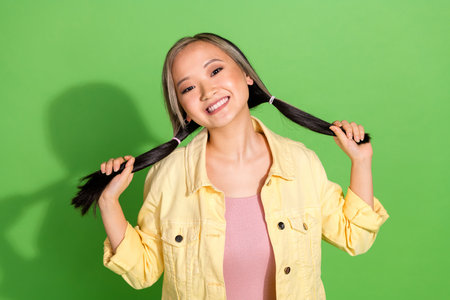Portrait of pretty young girl hands hold pull tails wear yellow jacket isolated on green color...