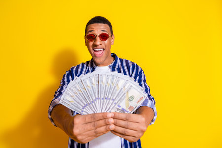 Photo of successful man with stylish haircut dressed striped shirt in sunglass show you money in hands isolated on vivid color background.の写真素材
