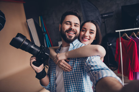Photo of smiling photographer taking selfie of adorable sweet lady wear red dress indoors studio...
