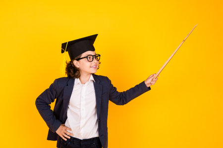 Photo portrait of little pupil boy stick pointer look empty space wear trendy uniform isolated on yellow color backgroundの写真素材