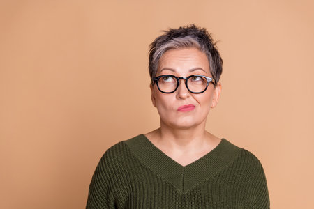Photo of minded woman with short hairdo dressed khaki knit sweater in glasses look at offer empty...