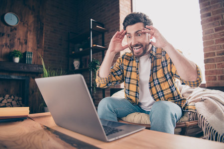Photo of handsome shocked guy wear plaid shirt having rest onlike sale shopping modern gadget indoors room home houseの写真素材