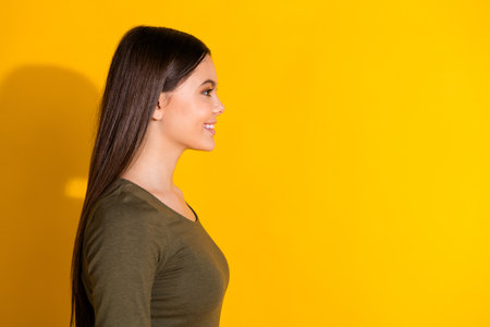 Photo portrait of pretty teenager girl profile look empty space wear trendy khaki outfit isolated on yellow color backgroundの写真素材