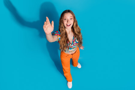 Full size high angle view photo of nice young girl arm wave wear top isolated on blue color backgroundの写真素材