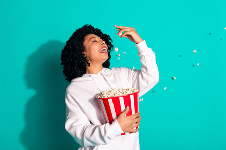 Photo portrait of wavy brunette hair girl in white hoodie going to cinema eating cheese pop corn bucket isolated on cyan color backgroundの写真素材