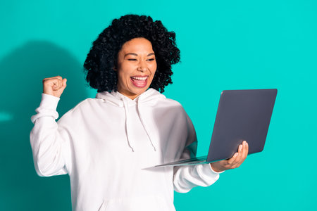 Photo of funny chevelure hairstyle lady wearing white hoodie holding laptop winning free spin gambling isolated on aquamarine color backgroundの写真素材