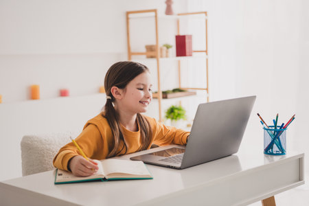 Portrait of smart schoolkid study laptop desk write notepad white interior apartment indoors
