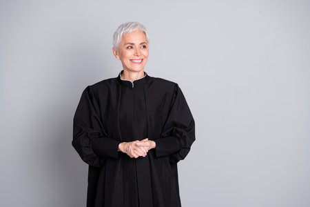Photo of smiling old woman judge look empty space wear black robe isolated grey color backgroundの写真素材