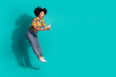 Full length photo of cheerful pretty lady dressed vintage t-shirt jumping high chatting gadget empty space isolated blue color backgroundの写真素材