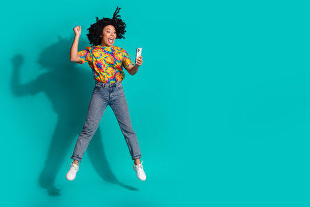 Full length photo of shiny lucky lady dressed retro t-shirt jumping high winning game gadget empty...