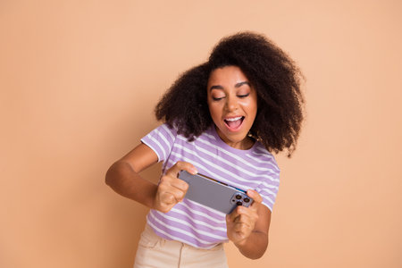 Photo of nice young woman play game smart phone wear striped t-shirt isolated on beige color backgroundの写真素材