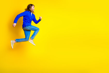 Photo of cheerful optimistic man wear trendy blue clothes jump up empty space isolated on yellow...