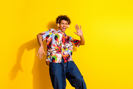 Portrait of nice funky young man dancing headphones wear shirt isolated on vibrant yellow color backgroundの写真素材