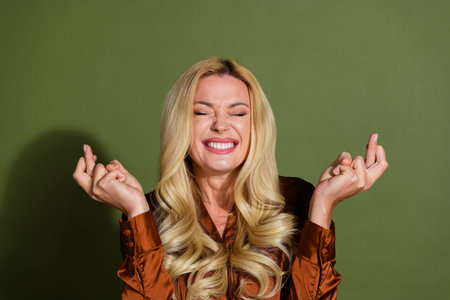 Photo of cheerful dreamy lovely woman wear satin stylish clothes crossed fingers isolated on khaki color backgroundの写真素材