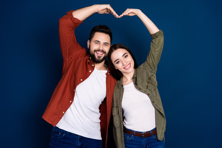 Photo of cheerful lovely nice wife husband wear stylish clothes heart sign isolated on dark blue...