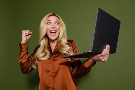 Photo of glad cheerful successful woman wear silky stylish clothes hold modern gadget isolated on khaki color backgroundの写真素材