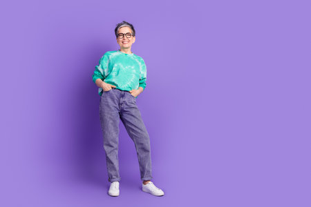 Full length photo of lovely pensioner lady posing hands pockets dressed stylish green garment isolated on purple color backgroundの写真素材