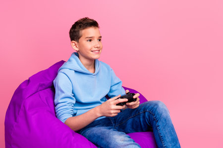 Photo portrait of funny teenager boy beanbag play videogame wear trendy blue outfit isolated on pink...