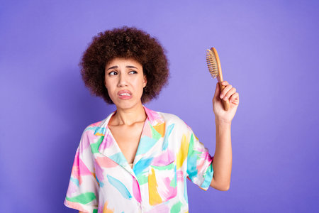 Portrait of nice young woman look arm hold hair brush wear shirt isolated on purple color backgroundの写真素材