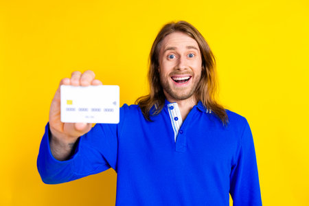 Photo of positive nice man wear stylish blue clothes hold card isolated on yellow color backgroundの写真素材