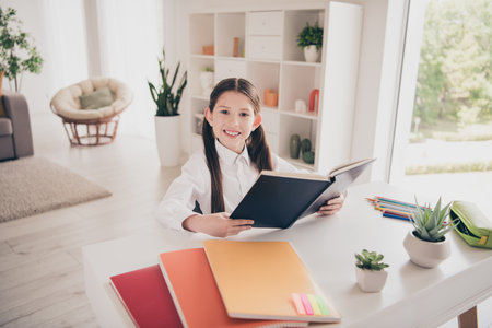 Photo portrait of small cute daughter reading book homework remote education home schooling isolated indoors backgroundの写真素材