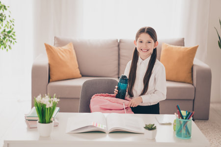 Photo portrait of small cute daughter packing rucksack water bottle remote education home schooling...