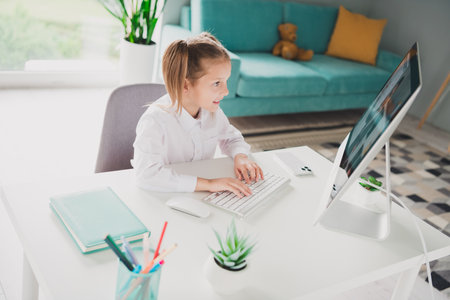 Photo portrait of cute small schoolgirl computer online lesson home education concept school interiorの写真素材