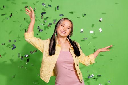 Portrait of pretty young woman dance confetti wear jacket isolated on green color backgroundの写真素材