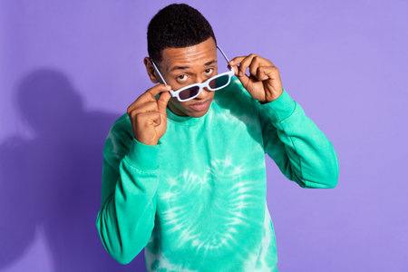 Photo of handsome suspicious guy wear teal sweatshirt arms dark glasses lookign you isolated purple...