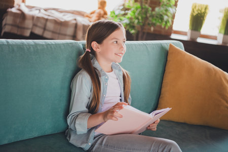 Portrait of cute little girl read book contemplate wear shirt loft interior modern flat indoorsの写真素材