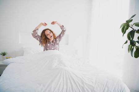 Photo of pretty young girl sit bed stretching yawning wear pajama bright interior bedroom apartment indoorsの写真素材