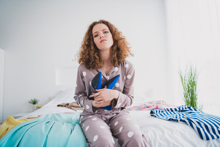 Portrait of nice young girl sit bed hold shoes wear pajama bright interior bedroom flat indoorsの写真素材