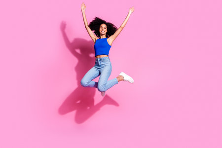 Full size photo of pretty young girl jumping raise hands wear trendy blue outfit isolated on pink...