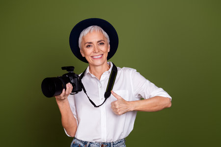 Photo of shiny attractive lady photographer dressed white shirt cap showing thumb up filming camera isolated khaki color backgroundの写真素材