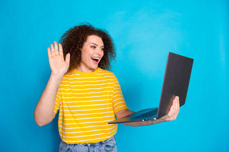 Photo of lovely young lady hold netbook video call wave hand dressed stylish striped yellow garment...