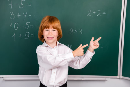 Photo of lovely small schoolboy point empty space dressed stylish uniform classroom blackboard...