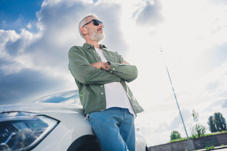Photo of confident positive guy dressed khaki shirt enjoying vehicle arms foded outdoors urban city streetの写真素材