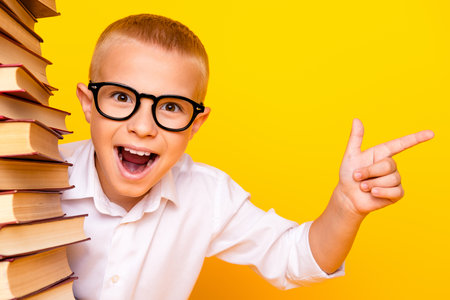 Photo of clever smart cheerful boy wear white shirt pile stack book empty space isolated on yellow...