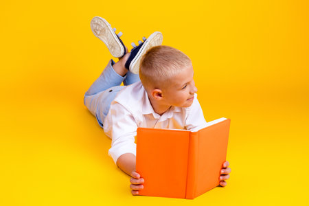 Photo of pretty cute intelligent boy wear white shirt read fiction story look empty space isolated on yellow color backgroundの写真素材