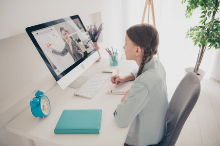 Photo of cute small girl study computer screen teacher desktop write notebook modern apartment indoorsの写真素材