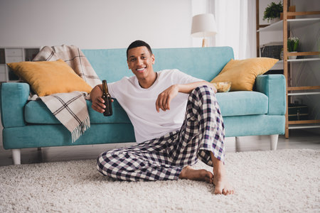Photo of attractive funny guy nightwear pajama watch football enjoying weekend couch drink alcohol indoors room home houseの写真素材