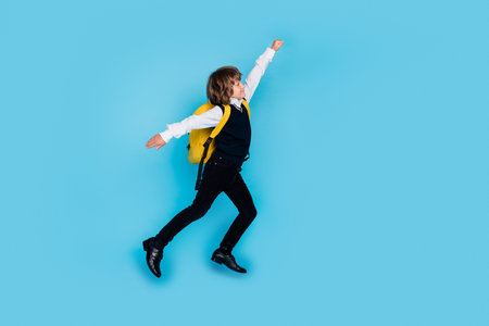 Full length portrait of little schoolchild boy jump empty space wear uniform isolated on blue color backgroundの写真素材