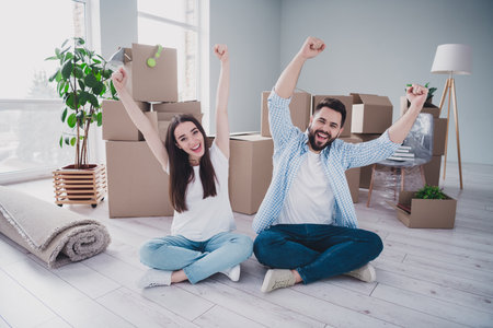 Full body portrait of two young people sit floor raise fists relocating moving box package new...