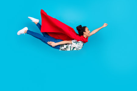 Full body portrait of lovely young girl superhero costume fly isolated on blue color backgroundの写真素材