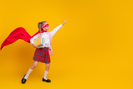 Full body photo of small schoolchild superhero costume uniform book empty space isolated on yellow color backgroundの写真素材