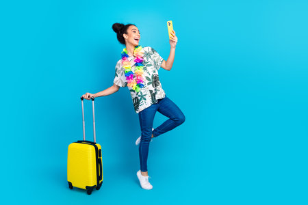 Full body portrait of lovely young girl suitcase smart phone empty space wear shirt isolated on blue color backgroundの写真素材