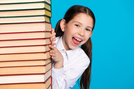 Photo of cute small schoolkid pile stack book empty space wear uniform isolated on blue color backgroundの写真素材