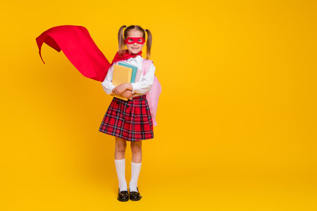 Full body photo of small schoolchild superhero costume uniform book empty space isolated on yellow color backgroundの写真素材